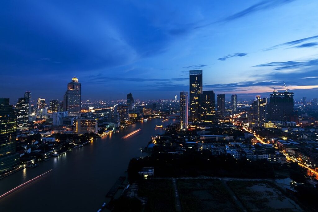 Vista area e noturna da cidade de Bangkok. O rio ao centro e prédios de ambos os lados.