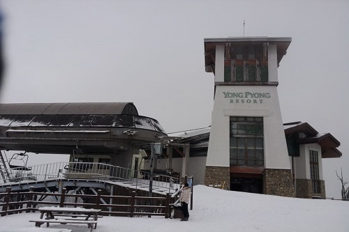 Entrada principal do Esqui em Yongpyong. Prédio branco com marron, em meio a neve.