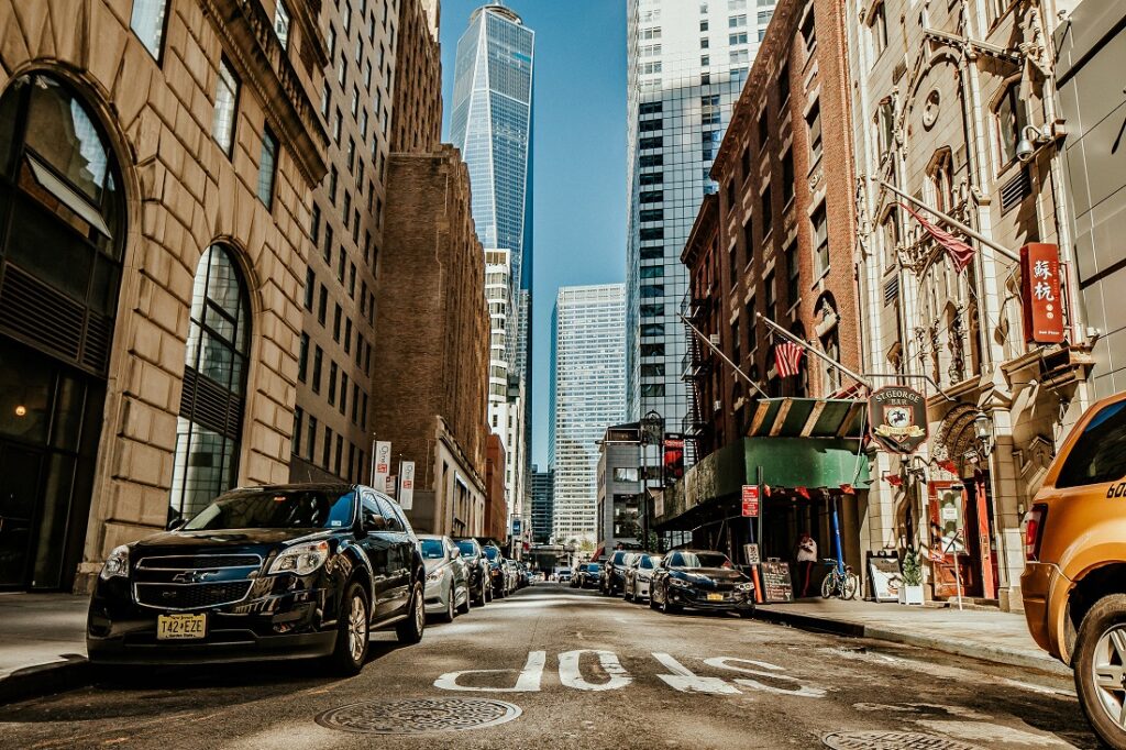 Avenida movimentada de Manhattan, com alguns carros passando e o One Trade Center ao fundo.