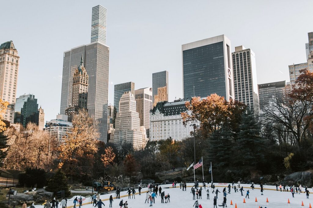 Pessoas patinando no lago congelado do Central Park, com os prédios de Manhattan ao fundo.