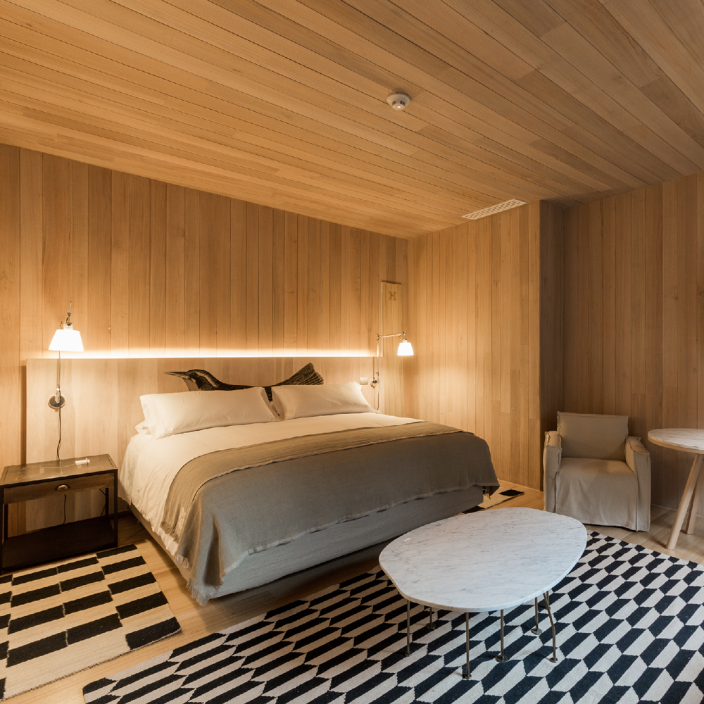 Acomodação do hotel magnólia. quarto com paredes revestidas de madeira, cama de casal e poltrona