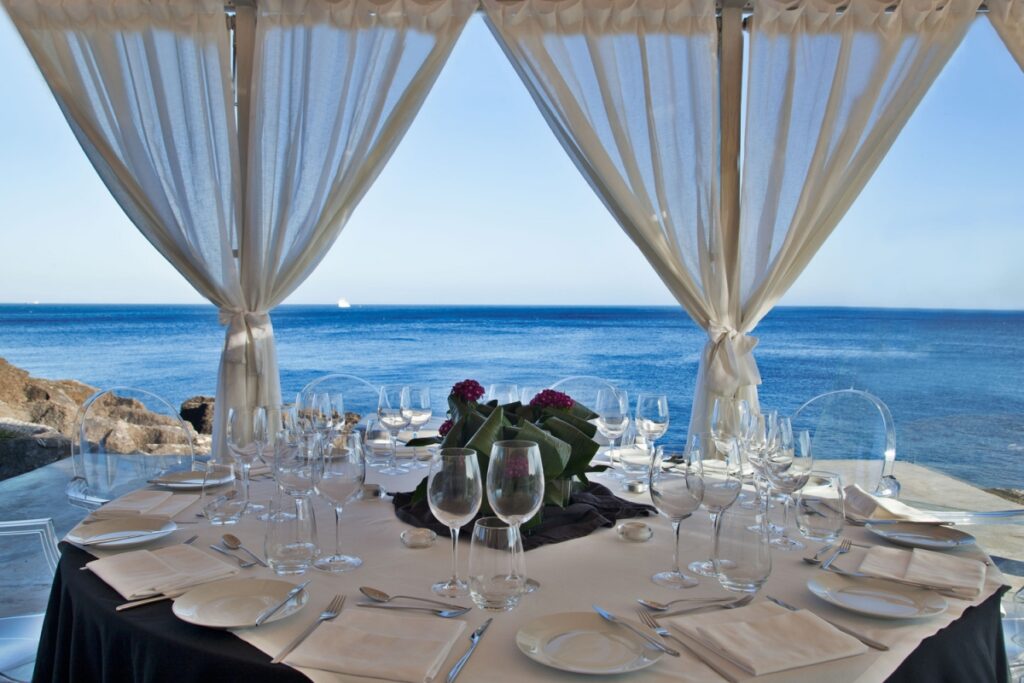 Mesa arrumada no restaurante do Farol Hotel, com vista panorâmica do mar.