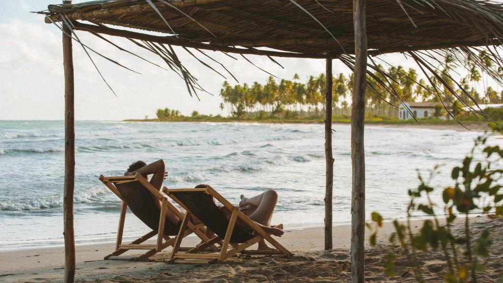 Casal deitado em espreguiçadeiras rústicas em bangalô da pousada Haya, um destino de luxo no nordeste em Miguel dos Milagres (Alagoas)