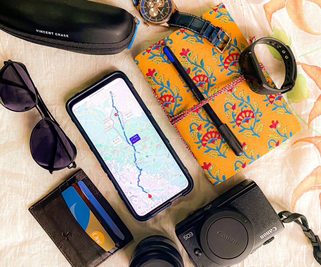 Objetos em cima da mesa - celular com tela do google maps para viagens, caderno, óculos escuros, carteira e relógios; 