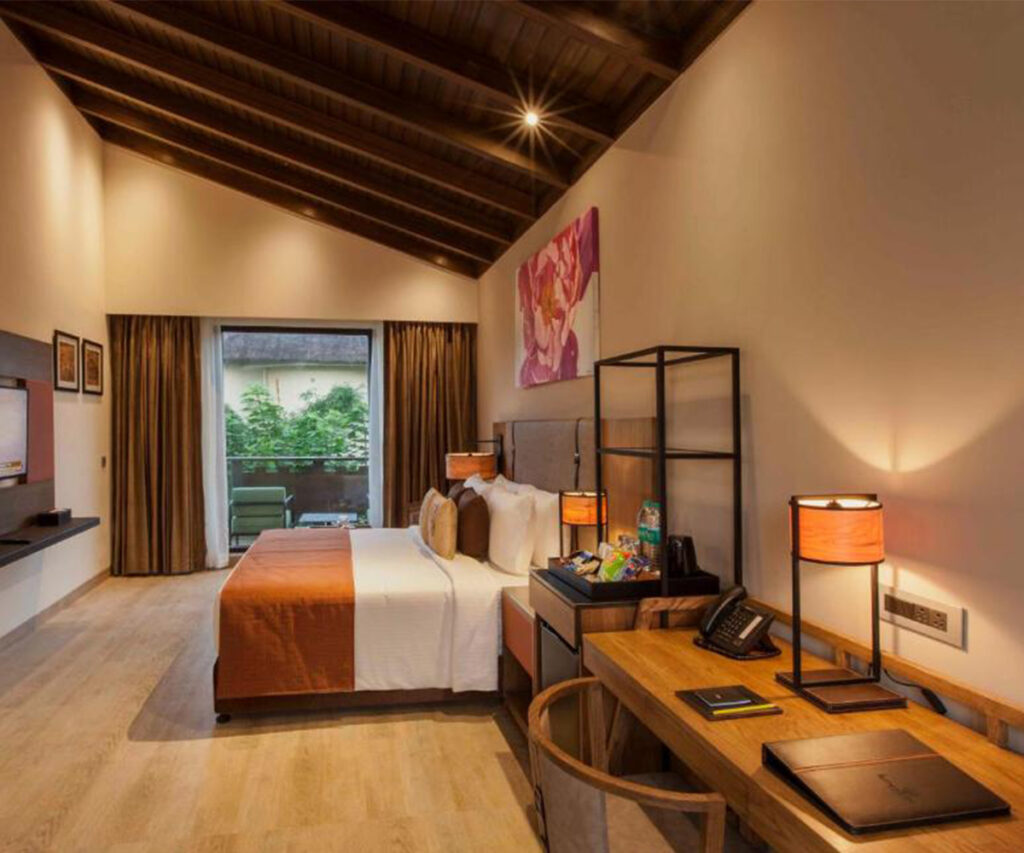 Quarto com varanda do lemmon tree premier - cama, eescrivaninha, televisão e teto de madeira com viga — um dos melhores hotéis na Índia