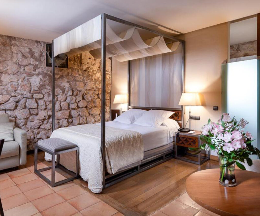 acomodação do parador alacón - cama de dossel, parede de pedras e mesa com flores