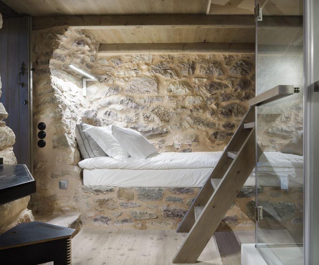 Quarto do tainaron blue - cômodo com parede de pedras, piso de madeira, escada e cama