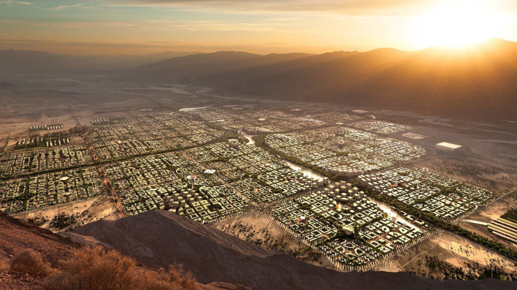A imagem apresenta uma vista aérea da Cidade Telosa projetada pelo grupo BIG de arquitetura. A paisagem urbana é caracterizada por um layout ordenado de edifícios e áreas verdes, com o sol se pondo ao fundo, lançando uma luz dourada sobre a cidade.