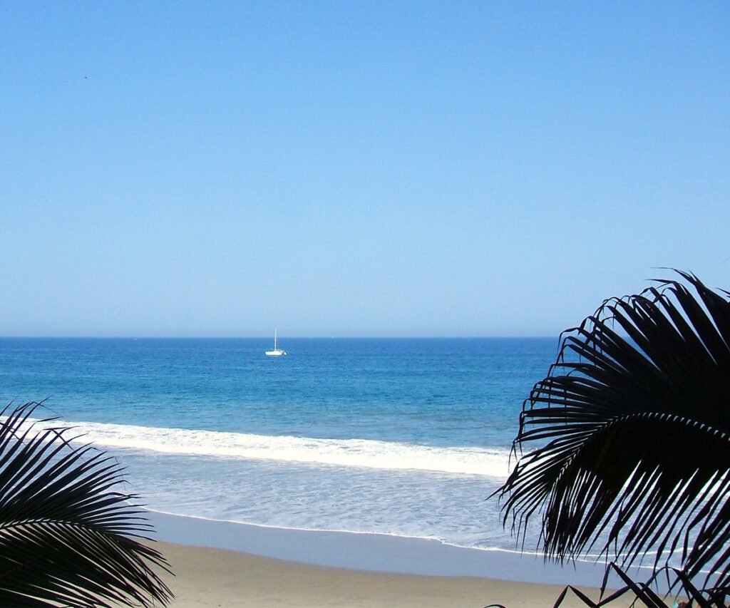 Melhor época para viajar para o Peru: praia de Mancora com palmeiras e barco ao longe