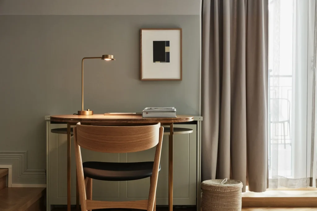 Home Office, decoração minimalista. O escritório apresenta uma mesa de madeira com uma cadeira combinando, iluminação de mesa e uma obra de arte na parede. A paleta de cores é neutra, com tons de verde claro e bege. A decoração é minimalista, com linhas limpas e um ambiente aconchegante.