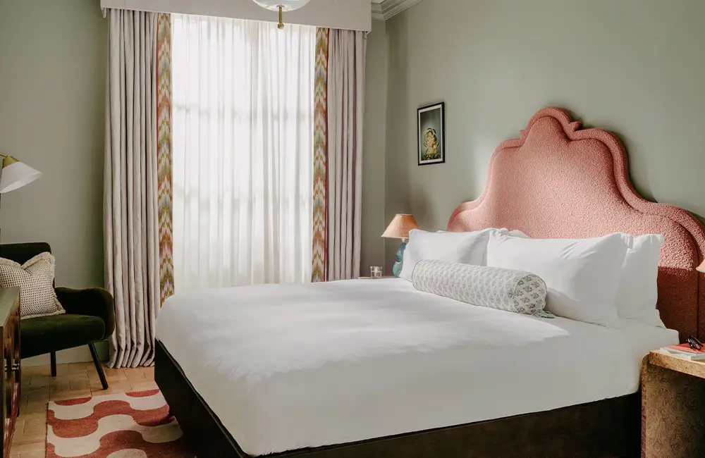 Quarto de hotel The Hoxton com cama branca e cabeceira rosa