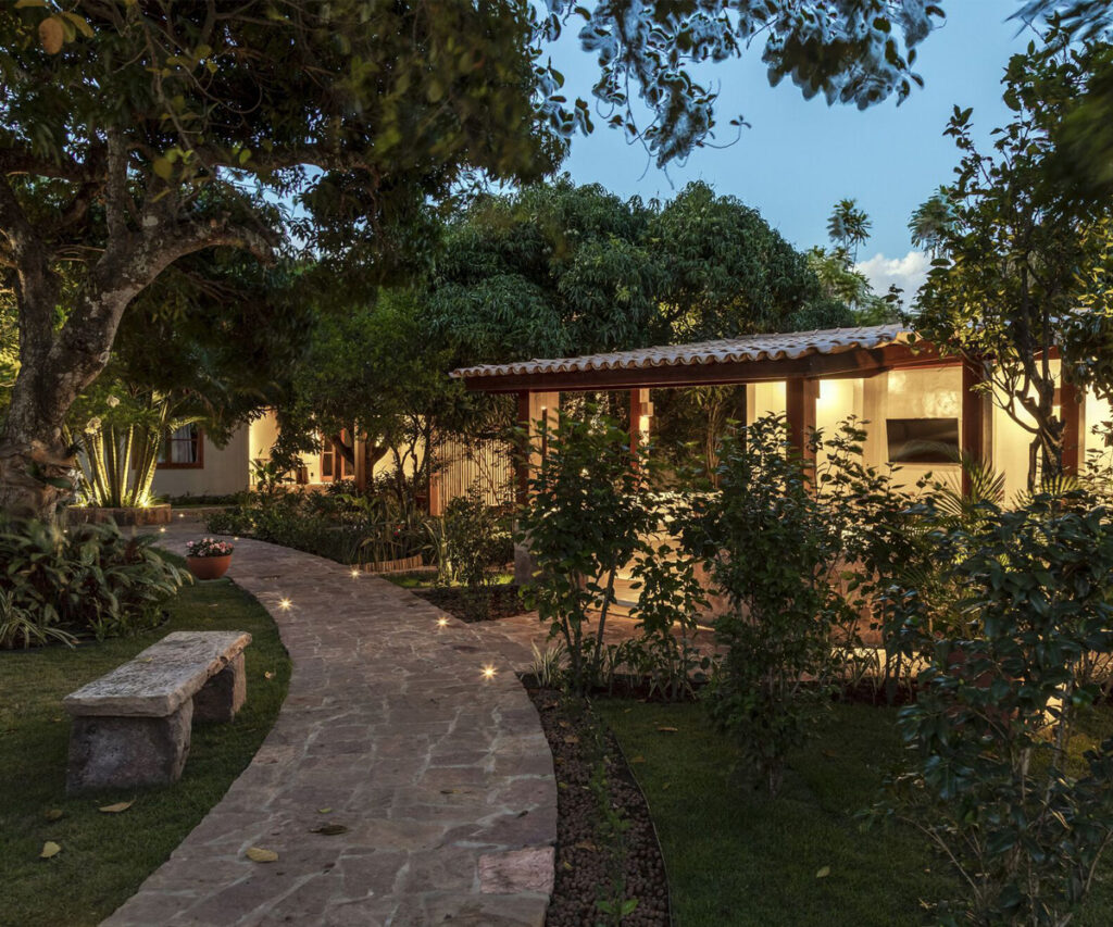 Jardim tropical brasileiro com caminho de pedra e casa de madeira