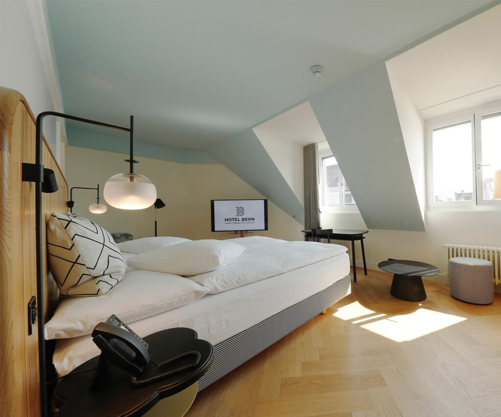 Hoteis em Berna: quarto moderno com cama branca e iluminação elegante.