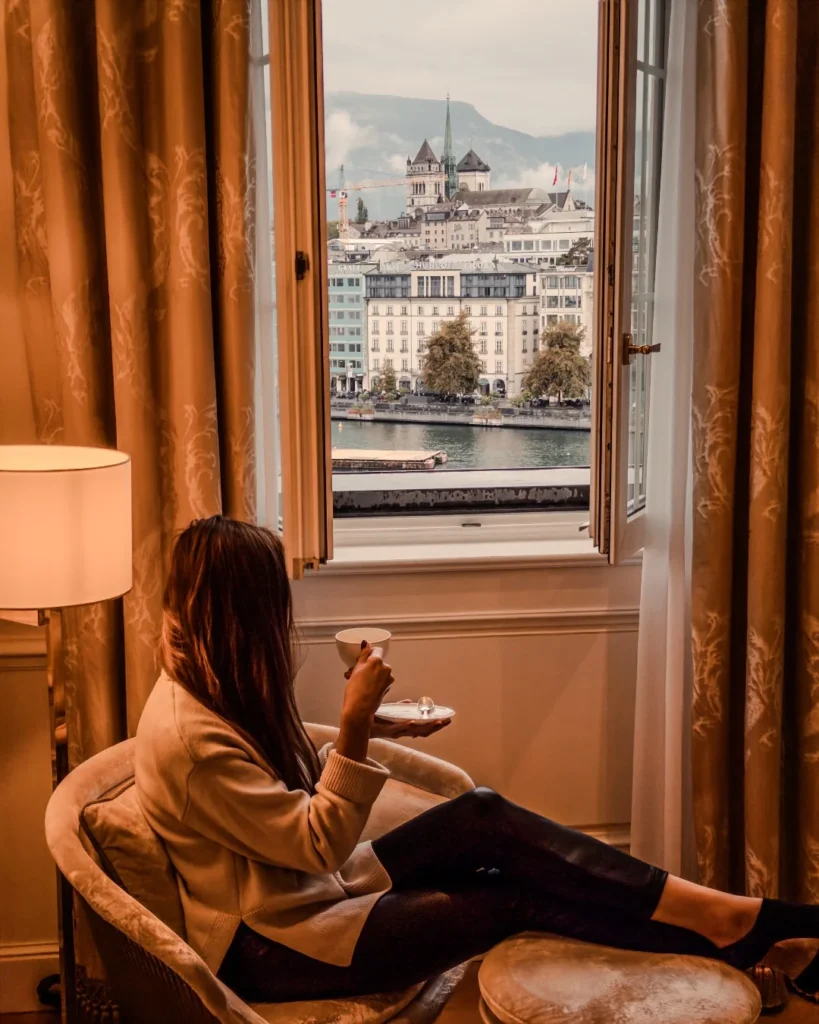 Mulher apreciando café em quarto luxuoso do Four Seasons Genebra com vista para o Rio Ródano e paisagem urbana