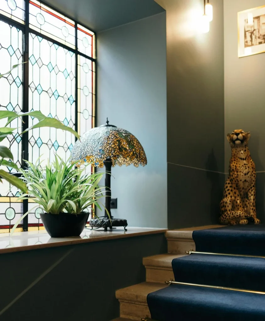 Hotéis em Genebra: interior do Hotel Longemalle com decoração clássica e moderna, incluindo escada com tapete azul e luminária de vidro colorido.