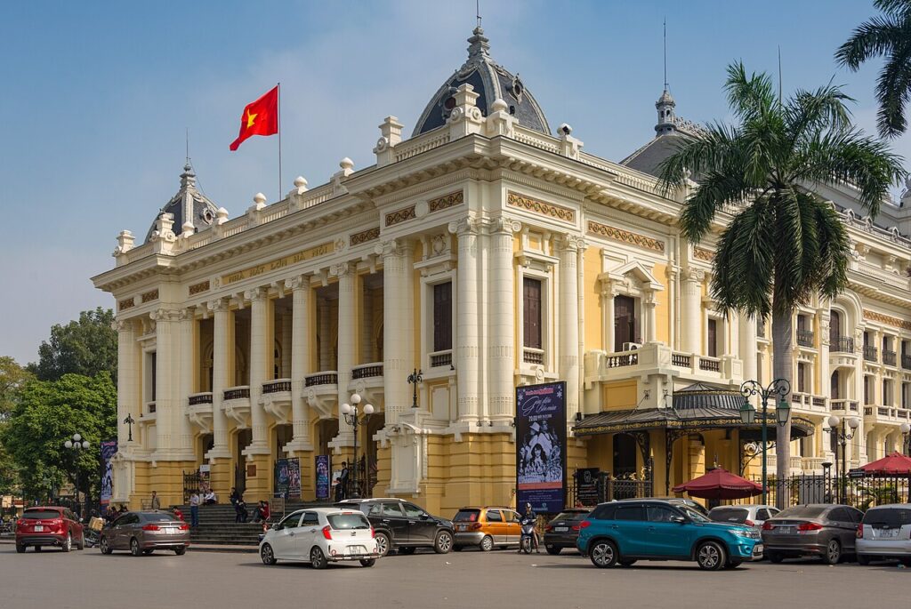 Ópera House de Hanói Vietnã: edifício histórico com bandeira vietnamita e carros em frente.