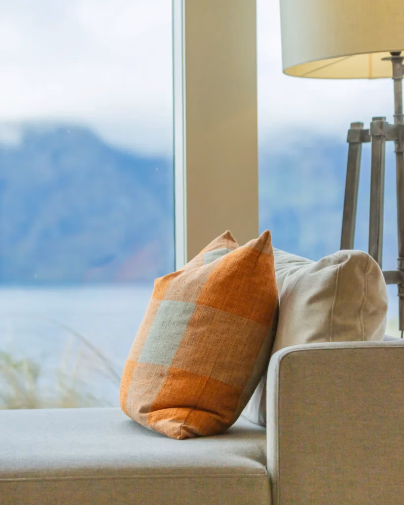 Viagem para Nova Zelândia: sofá elegante com vista panorâmica, almofadas neutras e detalhes rústicos, inspiração hotel premium (Rosewood Matakauri)