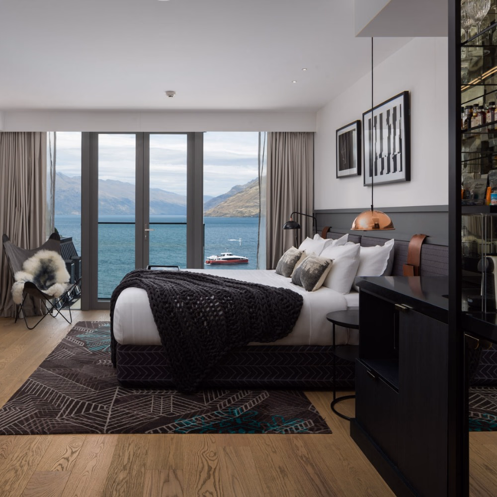 Viagem para Nova Zelândia: quarto luxuoso com vista para lago e montanhas, estilo moderno e elegante. Decoração sofisticada, ideal para relaxar após aventura. (125 caracteres)