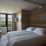 Quarto de hotel italiano com paisagem dos Dolomitas enquadrada por janela de esquadria preta, revestimento total em madeira de abeto.