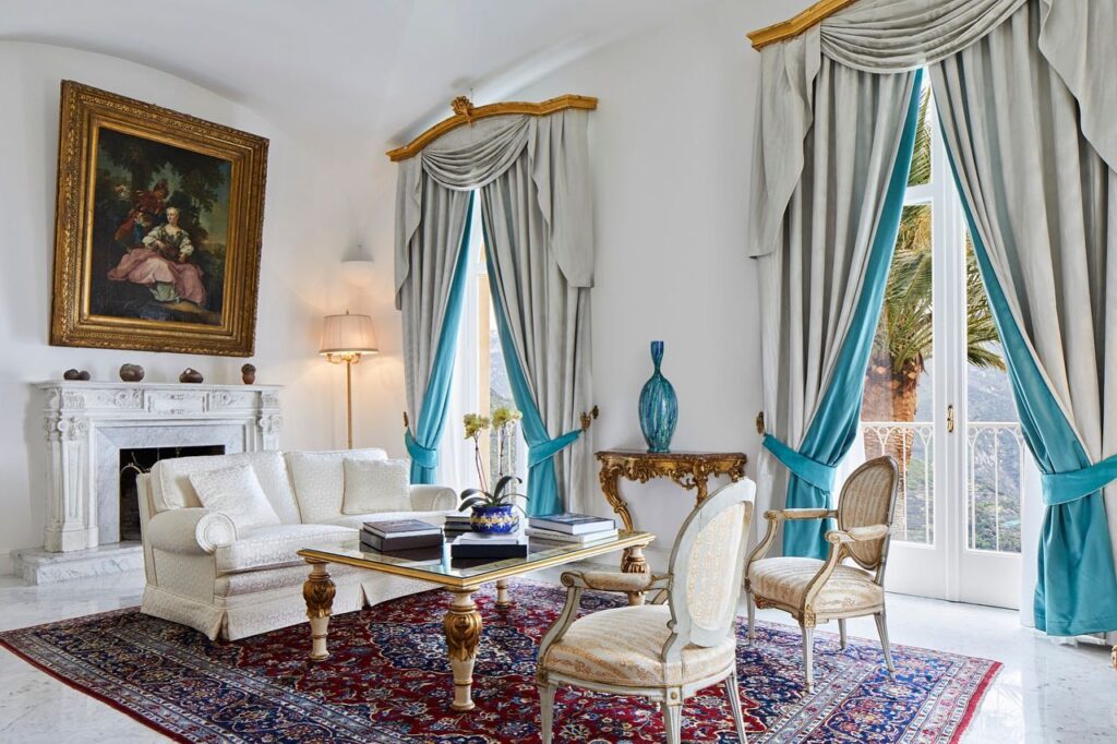 Salão clássico com lareira de mármore e cortinas elegantes em hotel de luxo, referência de onde ficar em amalfi com estilo histórico.