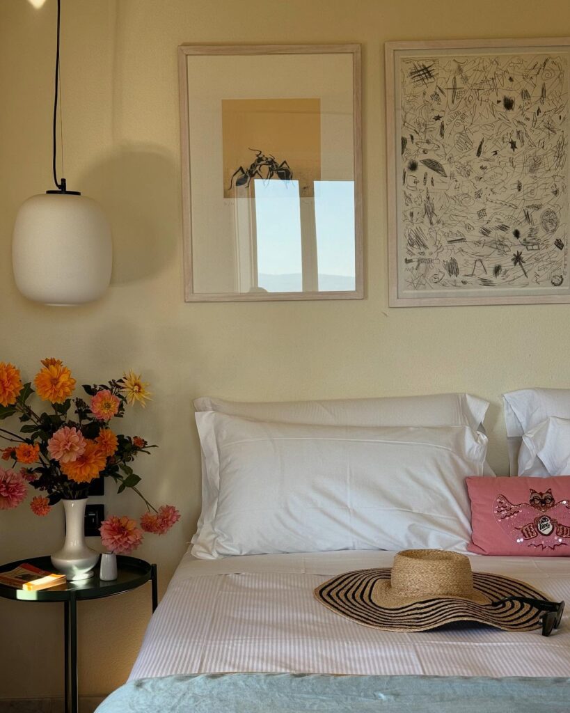 Quarto de hotel italiano com paisagem toscana, paredes amarelo-creme, obras de arte originais e flores frescas.