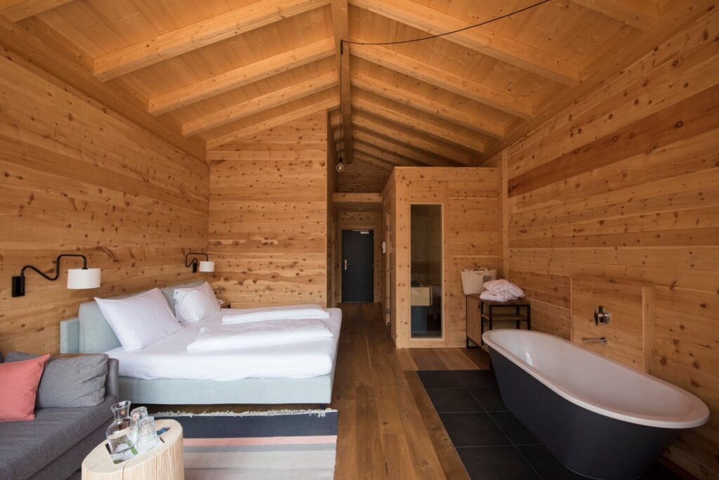 Interior de suíte de hotel italiano com paisagem alpina, sauna privativa embutida, banheira e teto de duas águas em pinho.