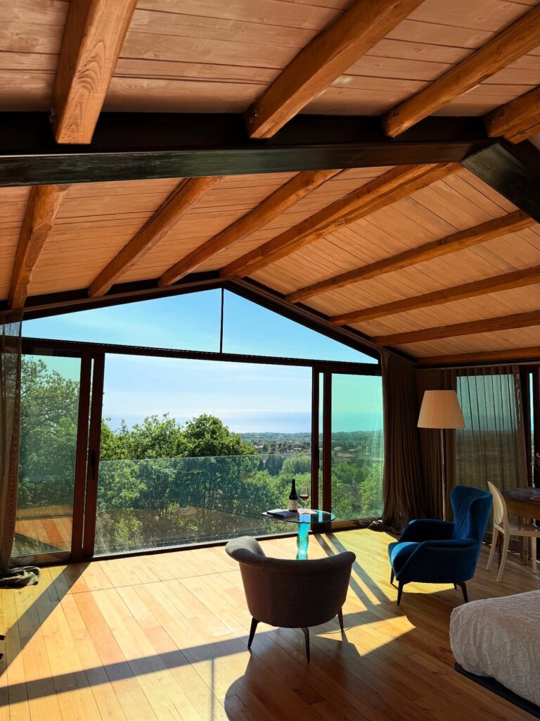 Área de estar de hotel italiano com paisagem para o mar, destacando arquitetura com teto de madeira e grandes painéis de vidro.