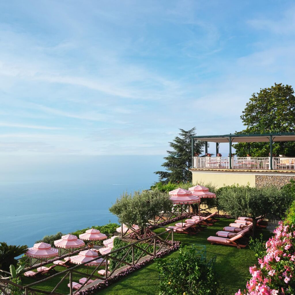 Terraço com guarda-sóis rosa e vista panorâmica para o Mar Mediterrâneo, uma experiência única de onde ficar em amalfi.