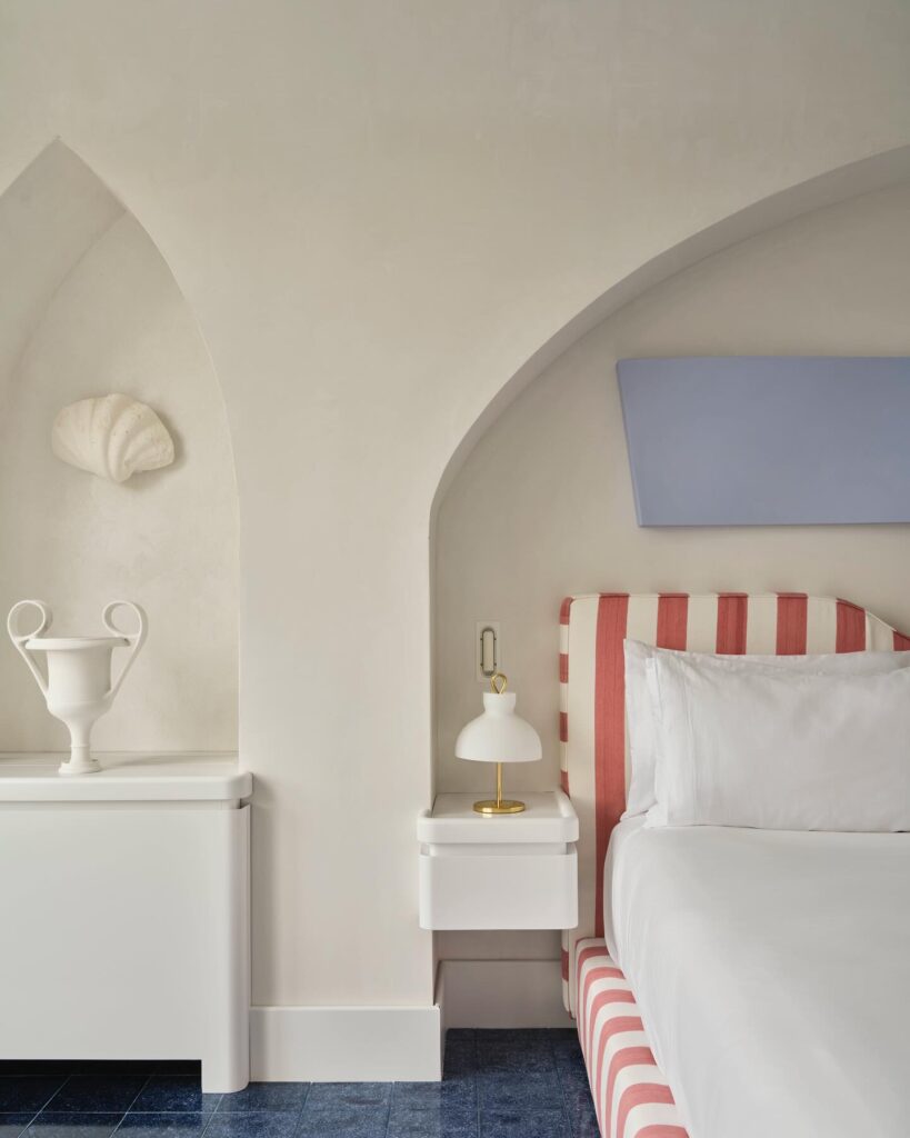 Quarto de hotel com cabeceira listrada coral e nichos arquitetônicos, conforto e design em onde ficar em amalfi.