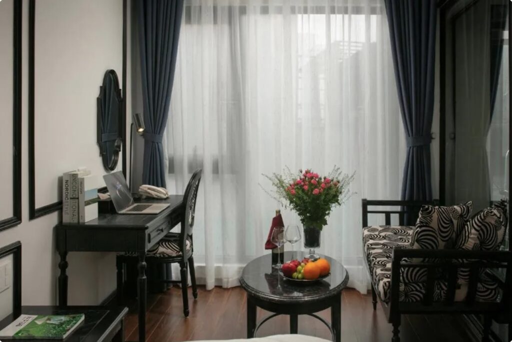 Área de estar em suíte de luxo com escrivaninha e poltrona decorada no Le Chateau Hotel, referência entre hoteis em hanoi.