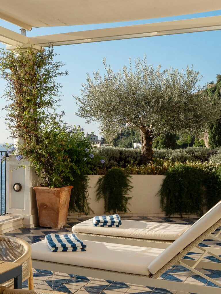 Área de lazer externa com espreguiçadeiras e oliveiras sob o sol, opção de onde ficar em amalfi.