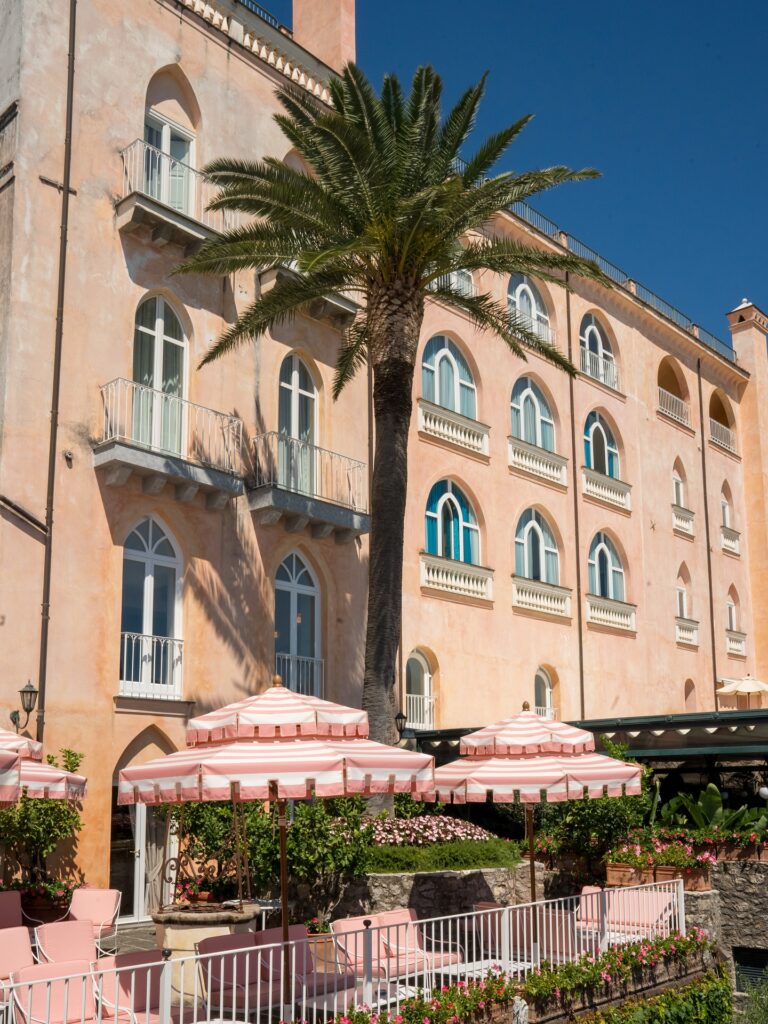 Fachada histórica de palazzo em tons de pêssego com palmeira, ícone de luxo de onde ficar em amalfi.