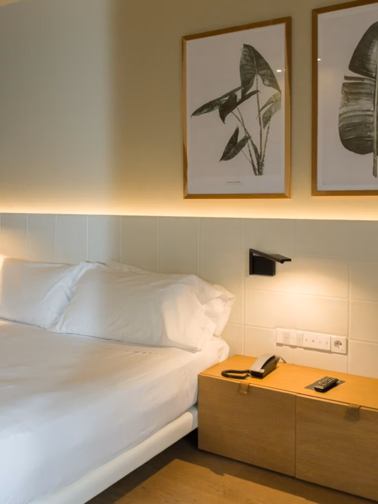 Detalhe de cabeceira e mesa de cabeceira em madeira no Arima Hotel & Spa San Sebastian com quadros botânicos.