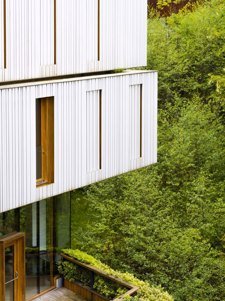 Fachada arquitetônica com brises verticais e janelas de madeira do Arima Hotel & Spa San Sebastian integrado à natureza.