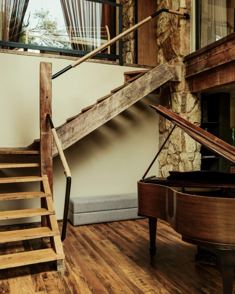 Ambiente interno com escada de madeira e piano, ideal como refúgio para a páscoa em meio à sofisticação rústica.