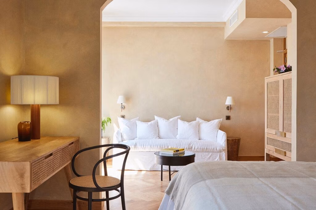 Suíte do Boutique Hotel Mendi Argia San Sebastian com paredes em terracota, sofá branco, cadeira Thonet e piso em parquet chevron sob luz suave.