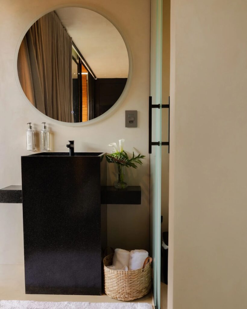 Banheiro minimalista com cuba preta e espelho redondo, ideal para um refúgio para a páscoa focado em design e relaxamento.