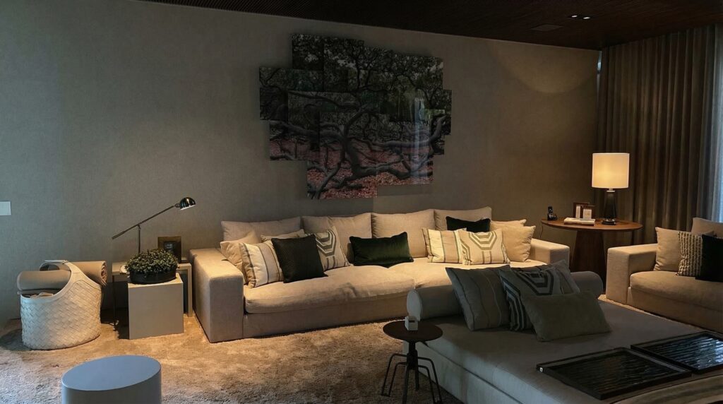 Sala de estar com sofá bege e almofadas em tons escuros sob iluminação quente, representando uma decoração de interiores elegante com forro de madeira.