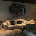 Sala de estar com sofá bege e almofadas em tons escuros sob iluminação quente, representando uma decoração de interiores elegante com forro de madeira.