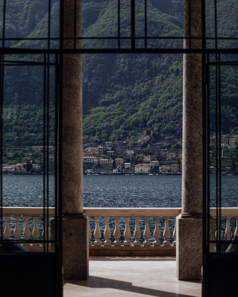 Portais de ferro e vidro emoldurando a vista para o Lago di Como com vilarejo e montanhas, Villa Làrio nos hotéis no lago di Como.