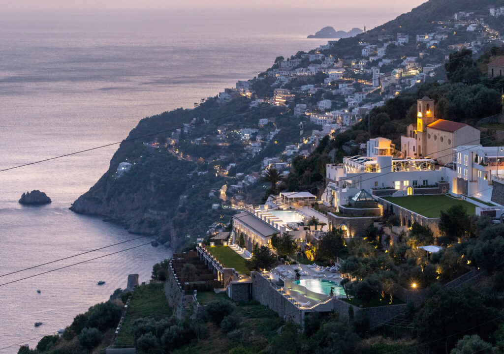 Hotel iluminado na encosta da Costa Amalfitana ao anoitecer, vista incrível de onde ficar em amalfi.