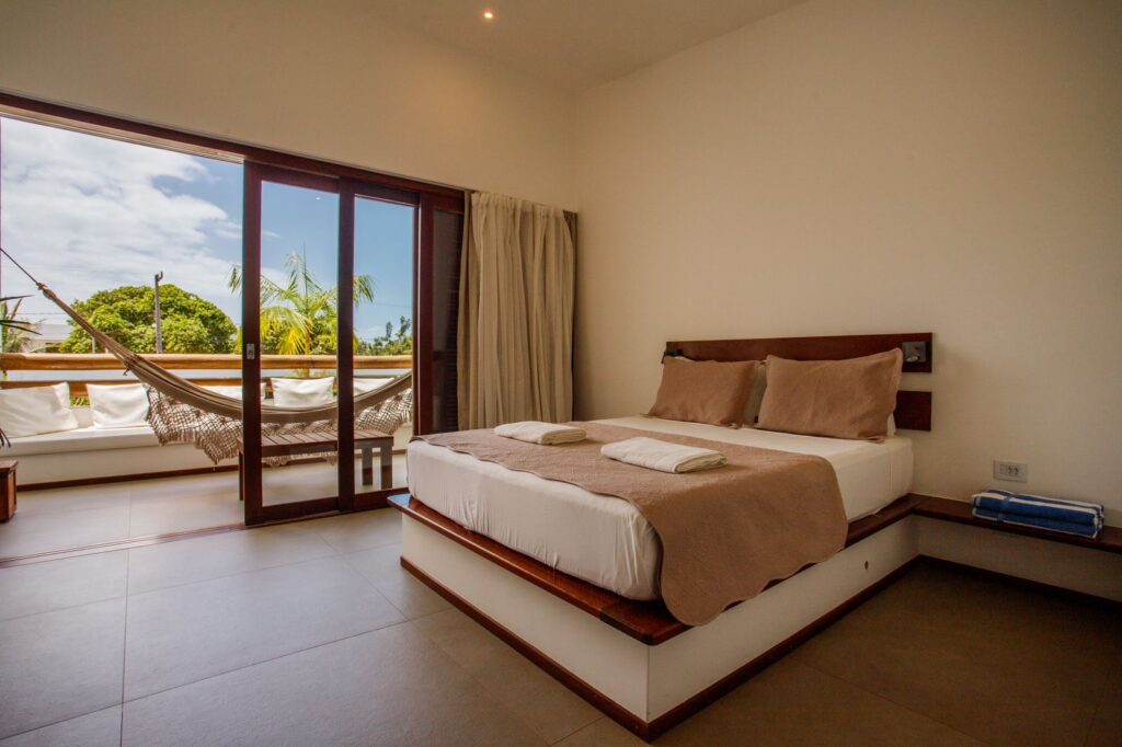 Suíte com cama de madeira e varanda com rede na Pousada Portofino, conforto e design autoral em hoteis em são miguel do gostoso.