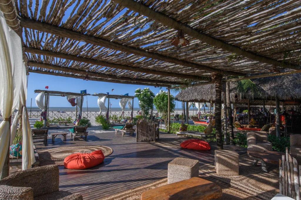 Deck externo do Rancho do Peixe com pergolado rústico, pufes coloridos e vista panorâmica para a praia do Preá.