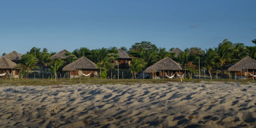 Bangalôs rústicos com teto de palha no Rancho do Peixe, cercados por coqueiros e areia branca no Ceará.