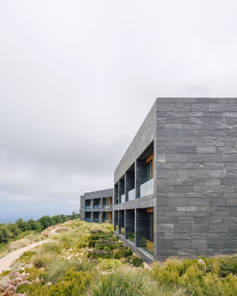 Fachada em pedra cinza e arquitetura contemporânea do Hotel Akelarre San Sebastian em meio à vegetação costeira.