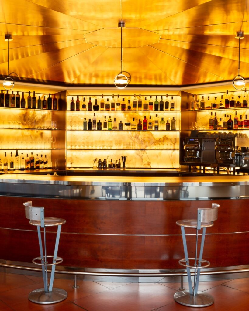 Bar Espazio Oteiza no Hotel Akelarre San Sebastian com teto dourado e prateleiras de pedra retroiluminadas.