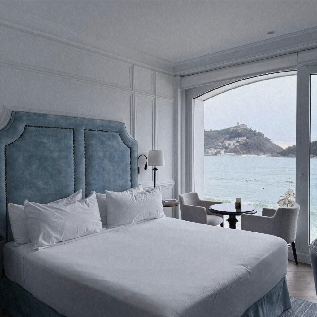 Quarto de luxo no Hotel Villa Favorita San Sebastian com cabeceira azul e vista panorâmica para o mar.