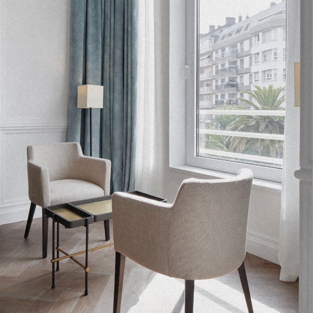 Canto de leitura no Hotel Villa Favorita San Sebastian com poltronas de tecido e cortinas azuis.