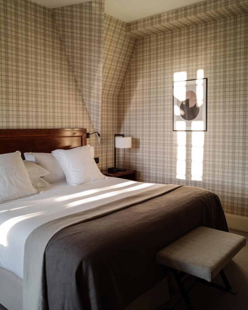 Quarto com papel de parede xadrez e iluminação natural suave no Hotel Villa Soro San Sebastian, apresentando uma estética acolhedora e atemporal.
