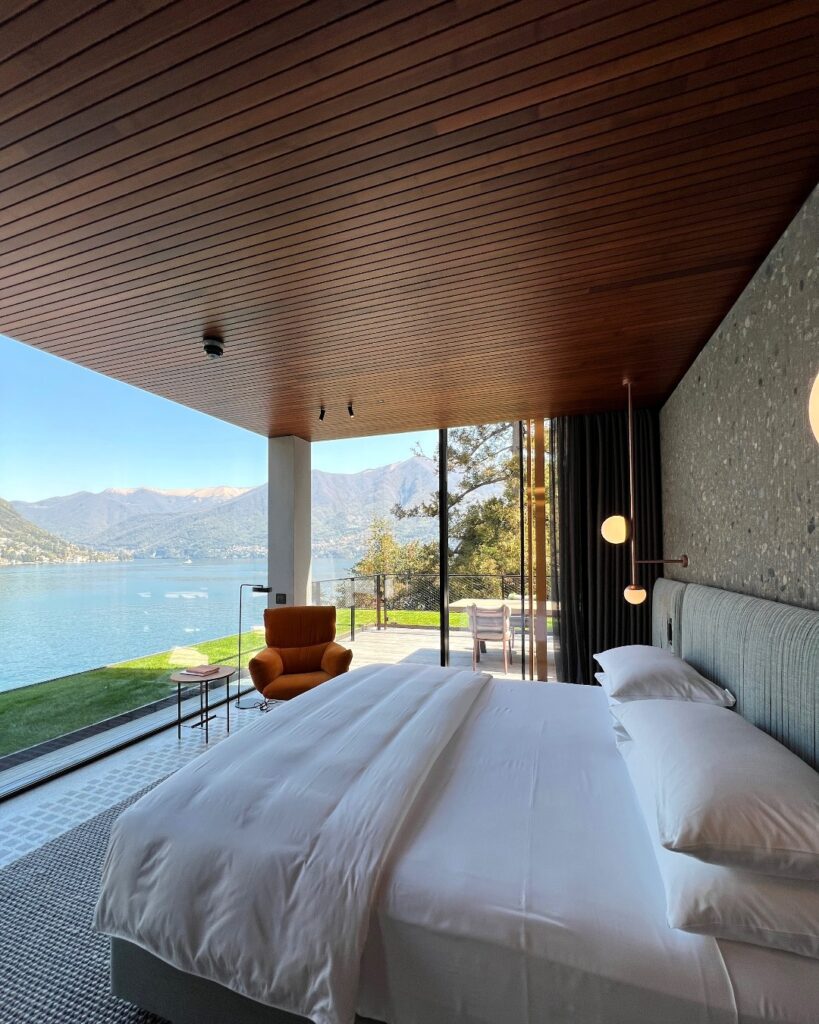 Suíte com teto ripado em madeira e fachada de vidro com vista direta para o Lago di Como, hotel de design italiano.